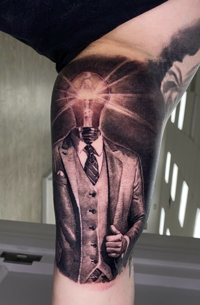 A Tattoo Depicting a Man in a Suit with a Light Bulb Design on His Leg